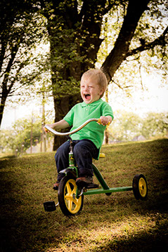 Tuscaloosa photographer picture of a boy riding his tricycle down a grassy hill.